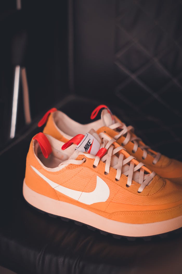 Stylish orange sneakers with white swoosh against a dark leather backdrop.